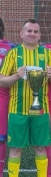 Simon stood with a football trophy outside in his football kit