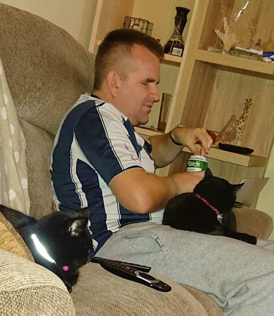 Simon sat on a sofa with two cats 