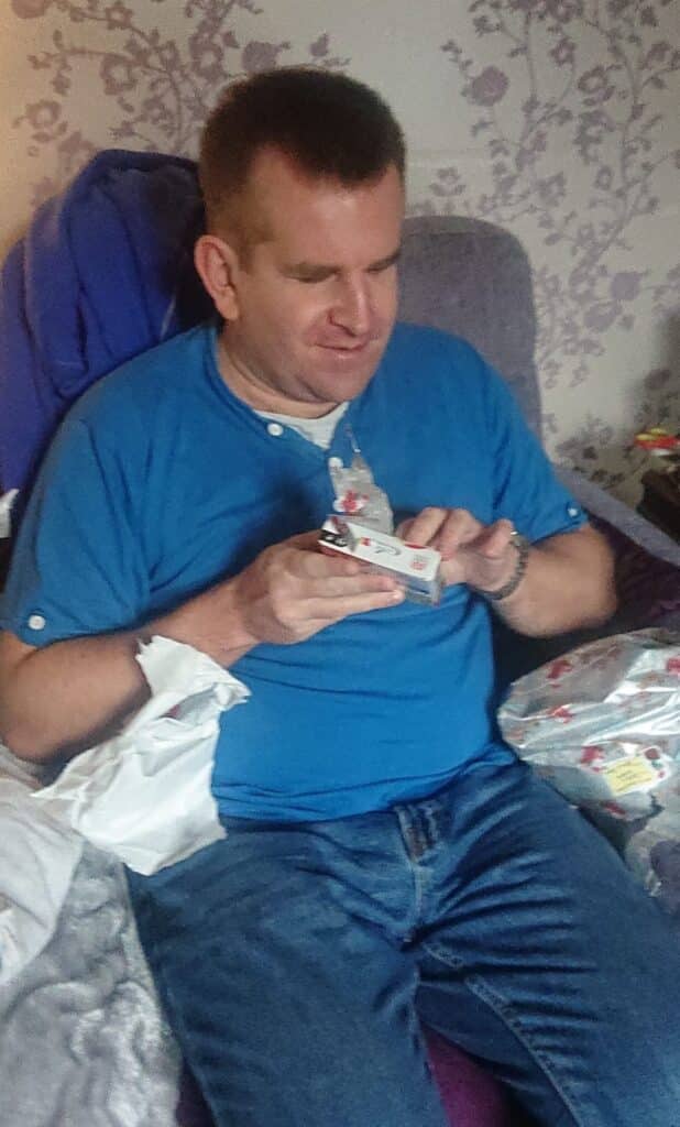 Simon smiling sat down opening up a present