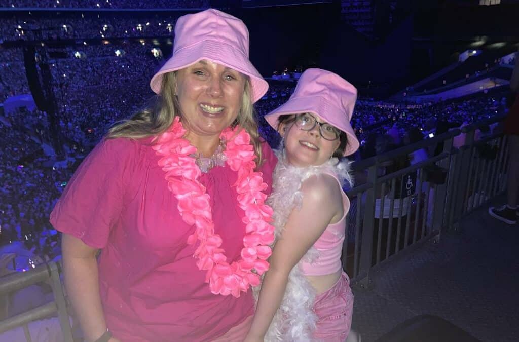 Both Kerrie and Megan are wearing pink tops, hats and feather bowers, stood inside Wembley