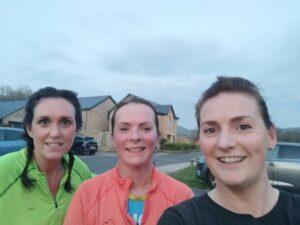 The three runners are smiling outside at the camera