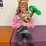 A girl is holding a balloon monkey on a balloon tree. She has face paint on.
