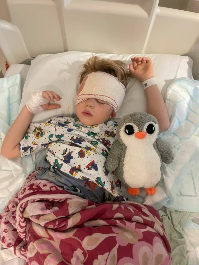 Arlo asleep at hospital wearing a bandage, lying next to Pip the penguin