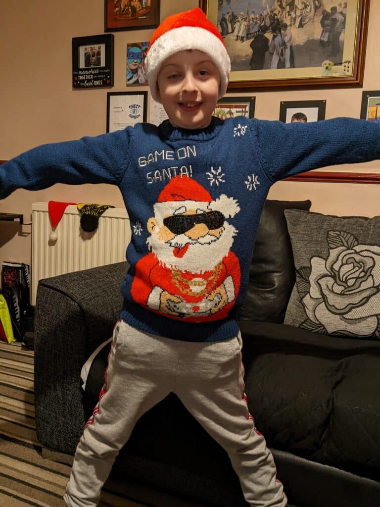 Sam is wearing a santa hat and Father Christmas jumper and smiling in a star shape
