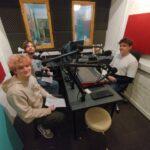 The group are sat inside the podcasting pod