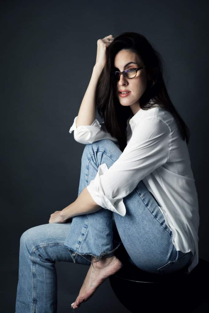 Ana is sat on a chair wearing a white top and jeans