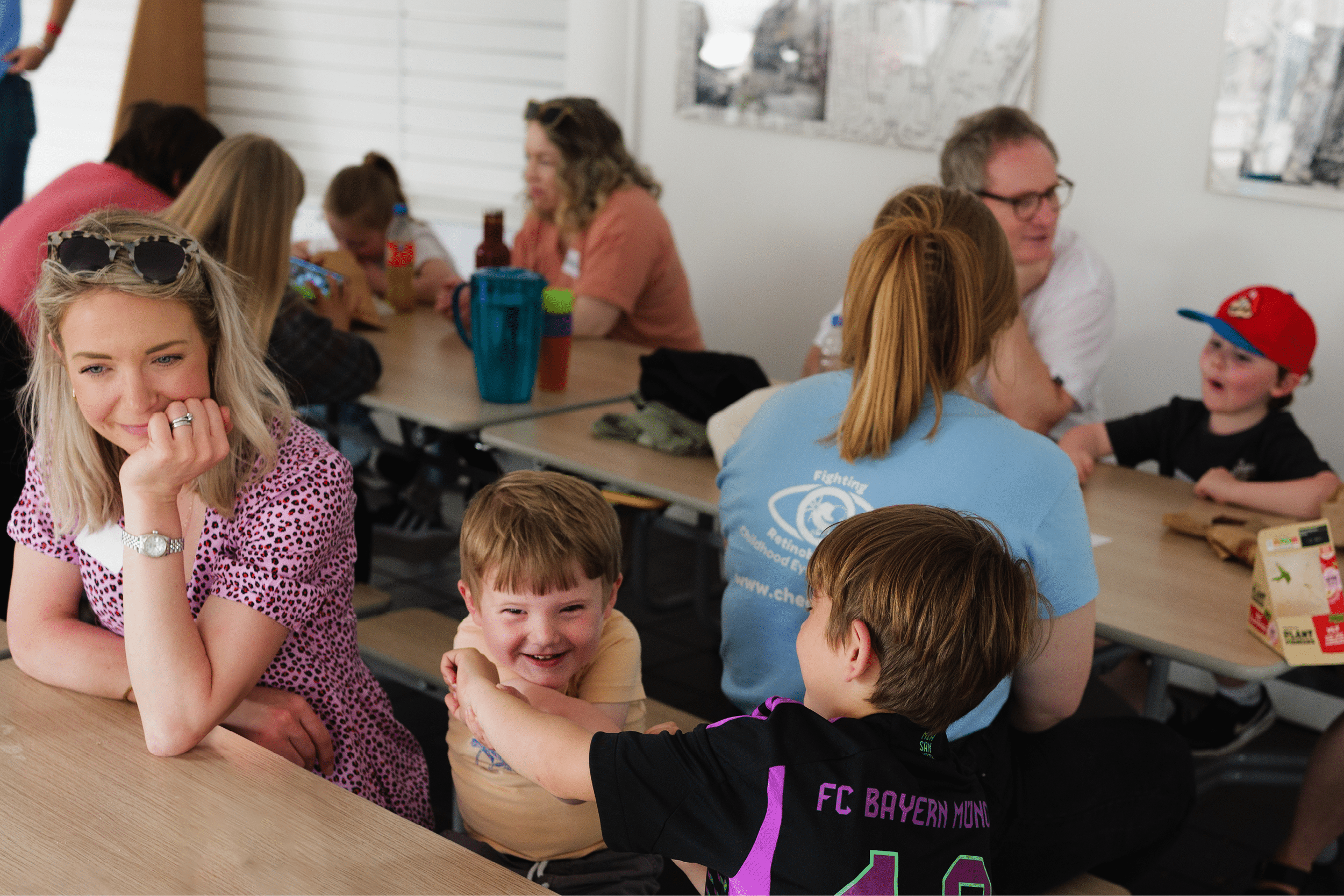 Group shot of families sitting around picnic tables having a good time at a previous CHECT event. Two boys are playing together with their Mum watching over them in the foreground. 