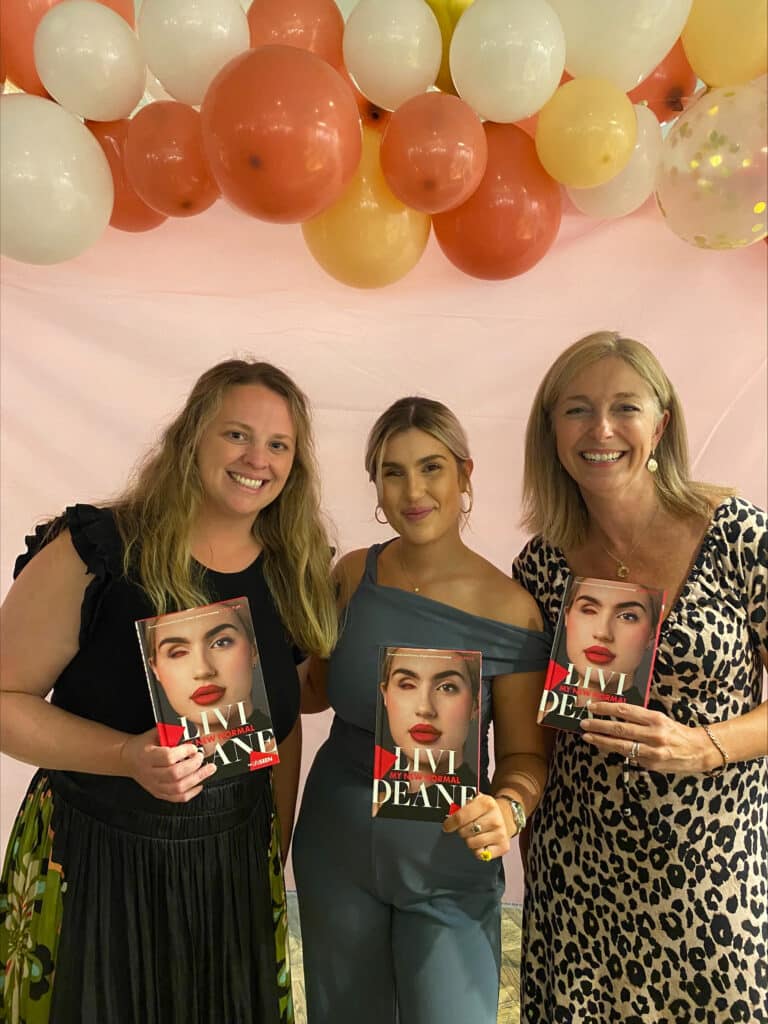 Livi, Isabella and Petra are stood against a balloon background all holding copies of the book