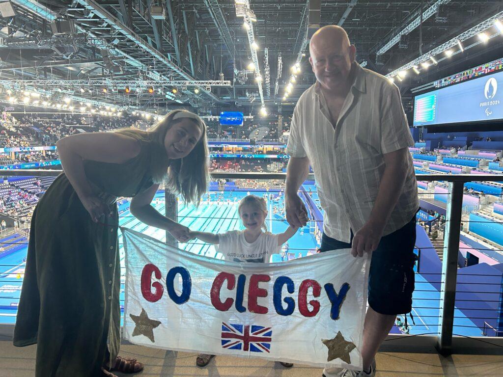 Adaline is holding a 'Go Cleggy' sign up at the Olympian stadium with two family members