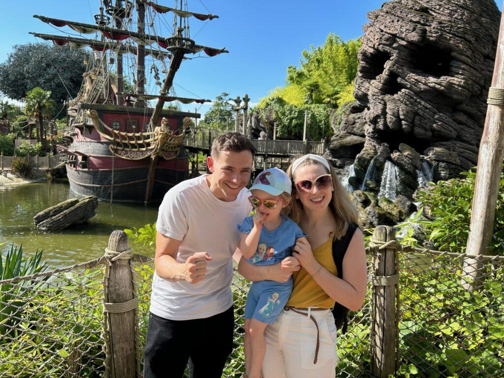Adaline is stood in front of a pirate ship with her parents at Disneyland Paris