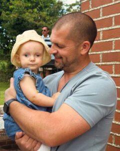 Craig is holding a baby while smiling at her