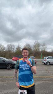 Tom is holding a medal in a CHECT running vest